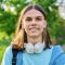 Outdoor portrait of handsome student guy with backpack looking at camera, green park campus background. Young smiling male with long hair hairstyle. Youth, education, young people concept
